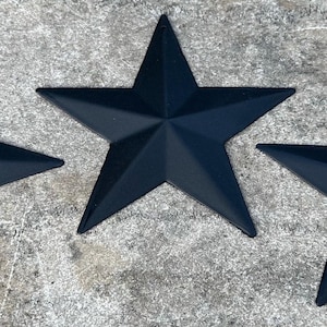May include: Three five-pointed stars with a matte black finish. Each star features a dimensional, raised center point that tapers out to five distinct arms. The stars are arranged in a horizontal row, displaying a uniform shape and color throughout.