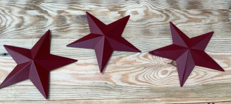 May include: Three red metal five-pointed stars on a wood background.
