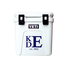 May include: White YETI cooler with black latches and the YETI logo. The front of the cooler features the initials "KDE" in navy blue, with "est. 2021" below. A durable, insulated cooler for outdoor activities.