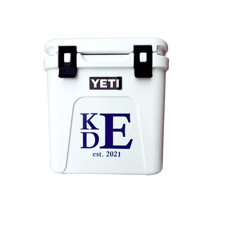 May include: White YETI cooler with black latches and the YETI logo. The front of the cooler features the initials "KDE" in navy blue, with "est. 2021" below. A durable, insulated cooler for outdoor activities.
