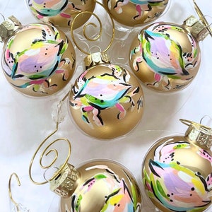 May include: Six gold Christmas ornaments with hand-painted abstract designs of crabs in shades of pink, blue, green, and black.