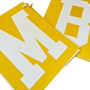May include: Yellow banner with white letters spelling out the word "M"