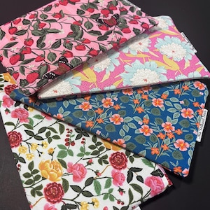 May include: Four rectangular fabric pouches featuring floral and botanical patterns. One pouch has a pink background with strawberries and butterflies, another has a pink background with light blue flowers, a third has a blue background with orange flowers, and the fourth has a white background with red, yellow, and pink roses.