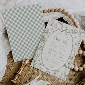 May include: Baby shower invitation set featuring a green and white gingham card and a matching invitation with a forest animal illustration. The invitation reads "A Sweet Little Baby Boy is on the way". A gold wax seal is also present.