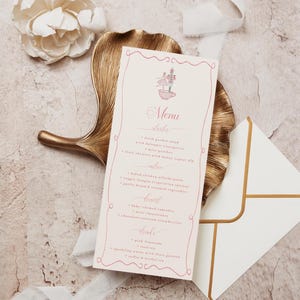 May include: A wedding menu with a pink floral design, featuring a list of dishes. The menu is on a gold leaf-shaped tray, with a white envelope and a white flower. The background is a textured, light-colored surface.