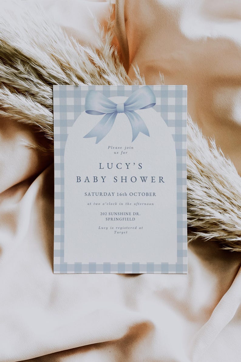 May include: A blue and white gingham baby shower invitation with a blue bow. The invitation reads "Please join us for Lucy's Baby Shower, Saturday 16th October at two o'clock in the afternoon, 202 Sunshine Dr., Springfield. Lucy is registered at Target."