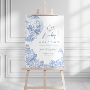 May include: Blue and white baby shower welcome sign with a hot air balloon and giraffe illustration. The text reads "Oh Baby! Welcome to the baby shower in honor of Gabriela Anderson, December 18, 20XX, Alexandria, VA."