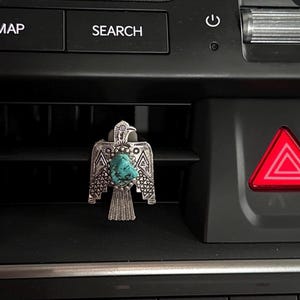 May include: A silver-toned metal ring shaped like a bird with outstretched wings, featuring an irregular, textured turquoise stone set in the center. The bird design includes intricate etched geometric patterns on the wings and tail feathers.