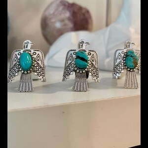 May include: Three silver-toned rings featuring a bird-shaped design with engraved wing patterns and a central turquoise stone. Each ring displays a unique natural turquoise cabochon, showcasing variations in color and matrix patterns on the bird.