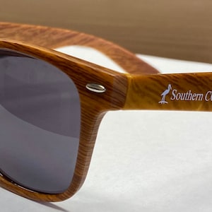 May include: Brown wood-framed sunglasses with dark lenses and the text "Southern Coastal" printed on the right arm.