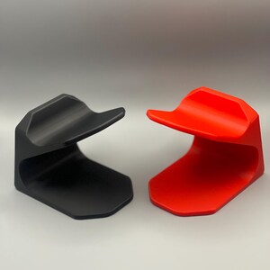 May include: Two 3D printed phone stands, one black and one red. The stands are designed to hold a phone upright.