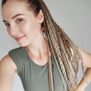May include: A sleeveless olive green ribbed top paired with a grey and black plaid skirt. The hair is styled in long, multi-tonal blonde and brown braided extensions that fall over the shoulder, complemented by a single dangling copper-toned earring.
