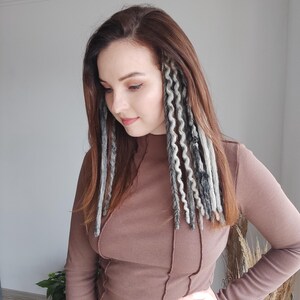 May include: A woman with long brown hair wearing a brown long-sleeved shirt. She has gray and black dreadlocks extensions in her hair.