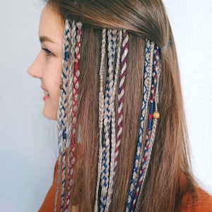 Könnte beinhalten: Eine Frau mit langen braunen Haaren hat mehrere Zöpfe in ihr Haar geflochten. Die Zöpfe sind in verschiedenen Farben, darunter Rot, Blau und Grau.