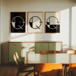 Pode incluir: Três impressões emolduradas em preto e branco da letra Q com um design circular. As impressões estão penduradas em uma parede branca acima de um armário verde claro e uma mesa de madeira com cadeiras.