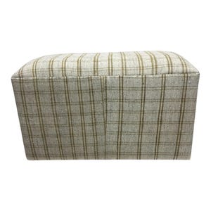 May include: A rectangular storage ottoman with a plaid fabric cover in shades of beige and brown.
