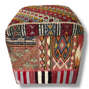 May include: A rectangular ottoman upholstered in a patchwork of woven fabric featuring various geometric patterns in red, blue, yellow, and cream. The top section is separated by a horizontal border, with vertical striped fabric at the base.