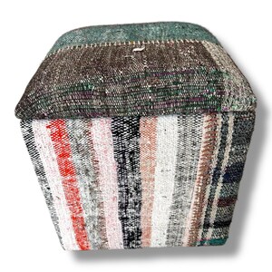May include: A square ottoman upholstered in a patchwork of woven textiles. The top features a dark brown and teal textured fabric, while the sides display vertical stripes in shades of red, white, pink, black, and gray with a woven finish.