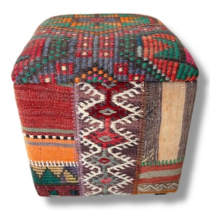 May include: A square ottoman upholstered in a patchwork of woven textiles featuring a variety of geometric patterns and colors including red, orange, green, blue, and beige. The top surface displays a grid-like design with repeating motifs.