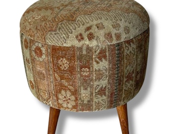 May include: A round ottoman featuring a textured fabric upholstery with a multi-colored pattern in shades of rust, beige, and brown. The seat is supported by three tapered wooden legs with a natural finish, providing a stable base for the stool.