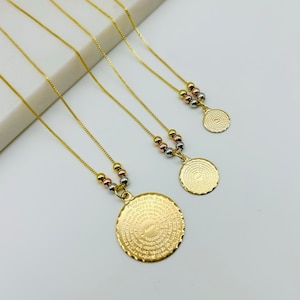 Puede incluir: Tres collares de oro de diferentes longitudes, cada uno con un colgante redondo con una inscripción circular. Los colgantes son de diferentes tamaños y los collares tienen tres pequeñas cuentas de diferentes colores.