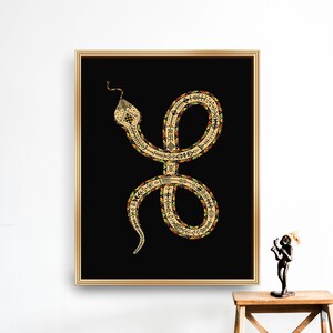 Könnte beinhalten: Eine goldene Schlange mit schwarzen, roten und grünen Markierungen auf schwarzem Hintergrund. Die Schlange ist zu einem Kreis zusammengerollt, mit erhobenem Kopf. Das Bild ist in Gold gerahmt.