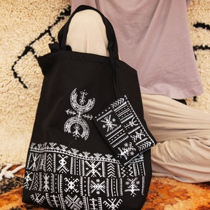 May include: A black tote bag with white geometric patterns and a smaller matching pouch. The bag has a long strap and is made of canvas.