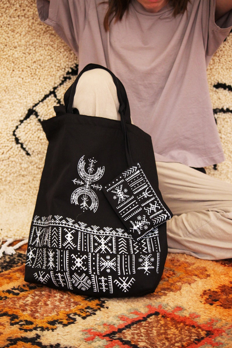 May include: A black tote bag with white geometric patterns and a smaller matching pouch. The bag has a long strap and is made of canvas.