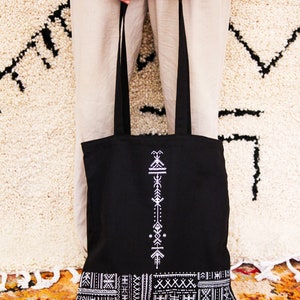 May include: Black tote bag with white geometric pattern. The bag has a long strap and a wide base.