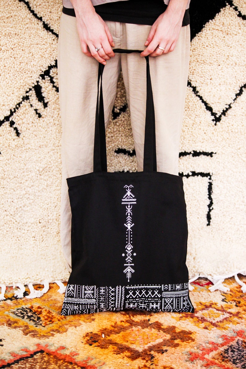 May include: Black tote bag with white geometric pattern. The bag has a long strap and a wide base.