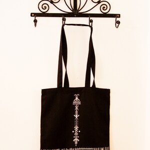 May include: Black tote bag with white geometric designs. The bag has a white embroidered pattern on the front and a white geometric border around the bottom.