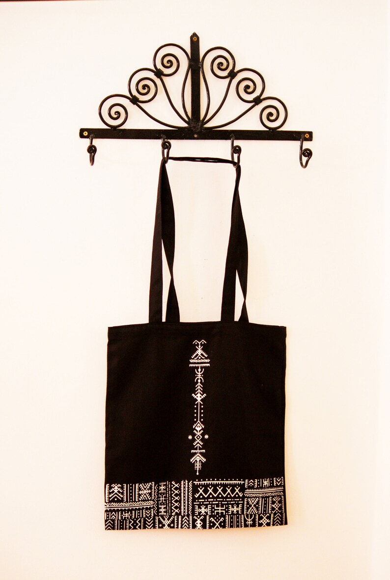 May include: Black tote bag with white geometric designs. The bag has a white embroidered pattern on the front and a white geometric border around the bottom.