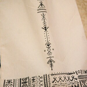 May include: A white canvas tote bag with black geometric designs. The design features a vertical pattern of triangles, diamonds, and dots. The bottom of the bag has a horizontal pattern of geometric shapes.