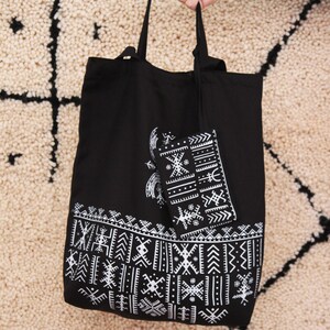 May include: Black tote bag with white geometric patterns. The bag has a smaller matching pouch attached to the inside.