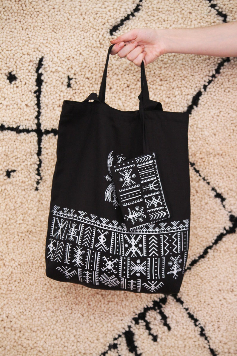 May include: Black tote bag with white geometric patterns. The bag has a smaller matching pouch attached to the inside.