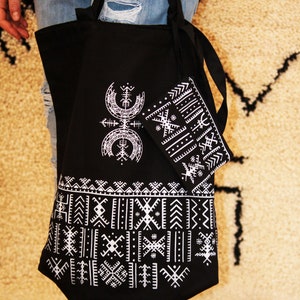 May include: A black tote bag with white geometric patterns and a smaller matching pouch. The bag has two long straps and is made of canvas.