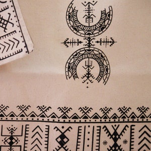 May include: A beige fabric with black geometric patterns. The fabric features a repeating border design and two larger, circular patterns in the center.