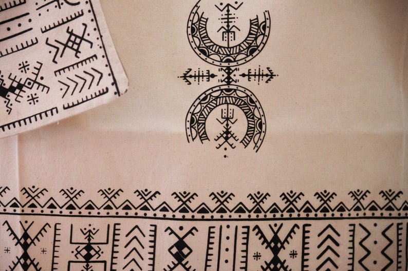 May include: A beige fabric with black geometric patterns. The fabric features a repeating border design and two larger, circular patterns in the center.