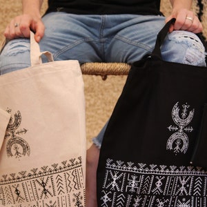 May include: Two tote bags with a geometric design. One bag is beige with black designs and the other is black with white designs.