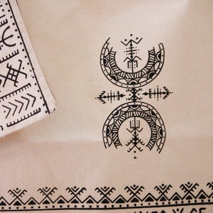 May include: A white canvas tote bag with a black geometric design. The design features two crescent moons with intricate patterns and a central symbol. The bag has a black and white geometric border.