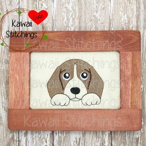 Puede incluir: Un perro beagle marrón y blanco asomándose desde un marco de madera. El marco está decorado con el texto "Kawaii Stitchings" y un corazón rojo con la palabra "Cute" en su interior.