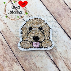 May include: Embroidered patch of a brown and white dog with its tongue sticking out. The dog is looking at the viewer with a happy expression. The patch is surrounded by a white border and has the text "Kawaii Cute Stitchings" on it.
