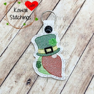 May include: A green and gold leprechaun keychain with a green hat, a shamrock, and a red beard. The keychain is made of felt and is attached to a silver key ring.