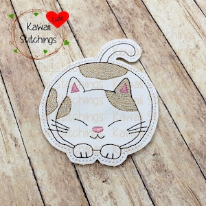 May include: White and brown embroidered cat with pink ears and a curled tail. The cat is curled up in a sleeping position. The embroidery is on a white fabric background.