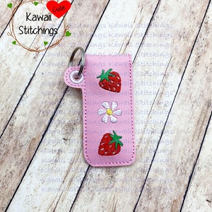 May include: Pink leather keychain with a key ring and embroidered strawberries and a flower. The keychain has the text "Kawaii Cute Stitchings" on it.