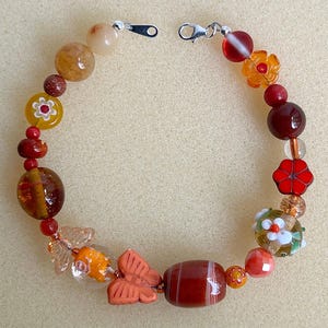 May include: A beaded bracelet featuring a variety of colorful beads. The bracelet includes orange, red, yellow, and clear beads, with flower and butterfly accents. The bracelet is secured with a silver clasp.