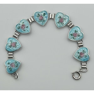 May include: A silver bracelet with heart-shaped links. Each heart is light blue with a pink rose design. The bracelet has a clasp closure. A charming piece of jewellery.