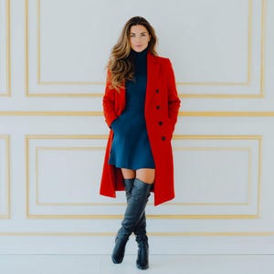 May include: A vibrant red long-sleeved coat with a notched lapel and black buttons worn over a dark blue turtleneck dress. The outfit is paired with black leather over-the-knee boots. The ensemble features a structured silhouette and solid colors.