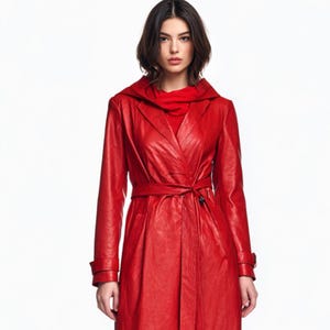 May include: A vibrant red leather trench coat with a matching belt and hood. The coat features long sleeves and a wrap-style closure. The model is wearing a red turtleneck underneath the coat.