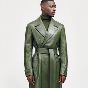 May include: Olive green leather trench coat with a matching belt. The coat features a classic double-breasted design with a notched collar and button details. The model is wearing a green turtleneck underneath.
